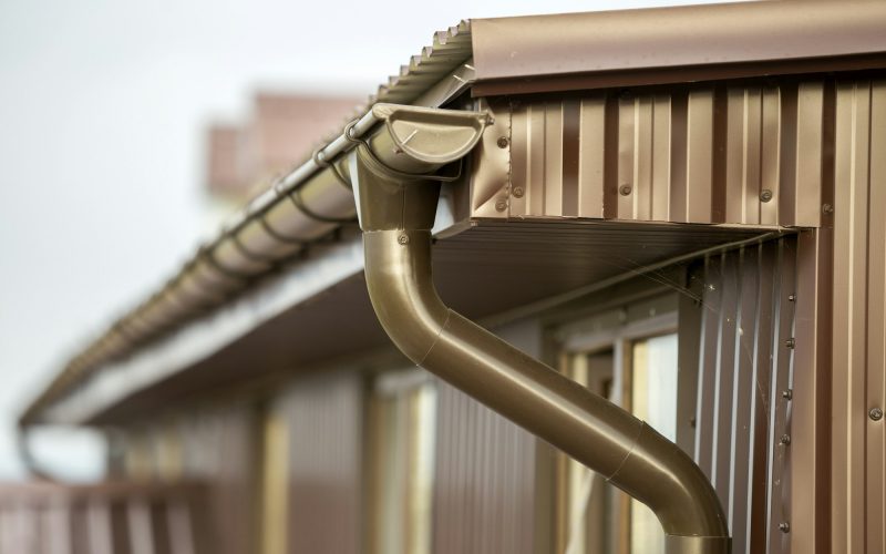 Close-up detail of cottage house corner with metal planks siding and roof with gutter rain system.