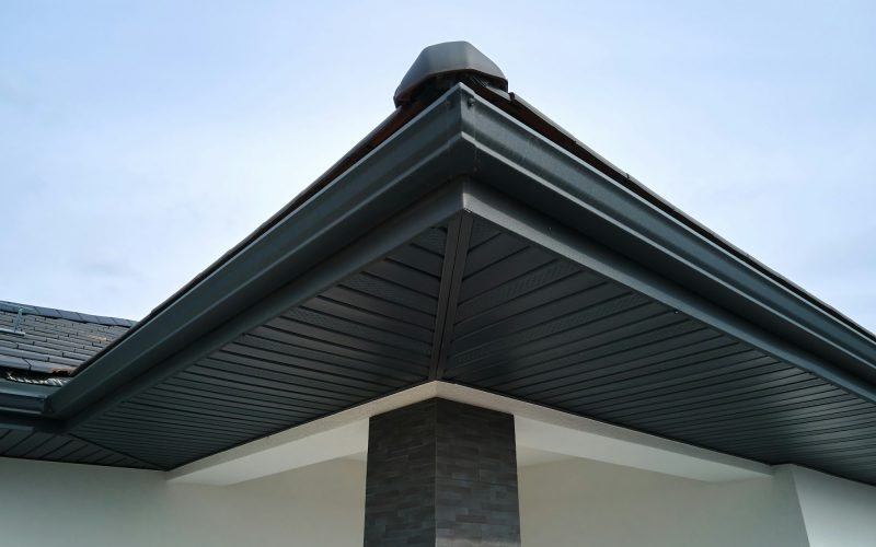 House corner with brown metal planks siding and roof with steel gutter rain system.